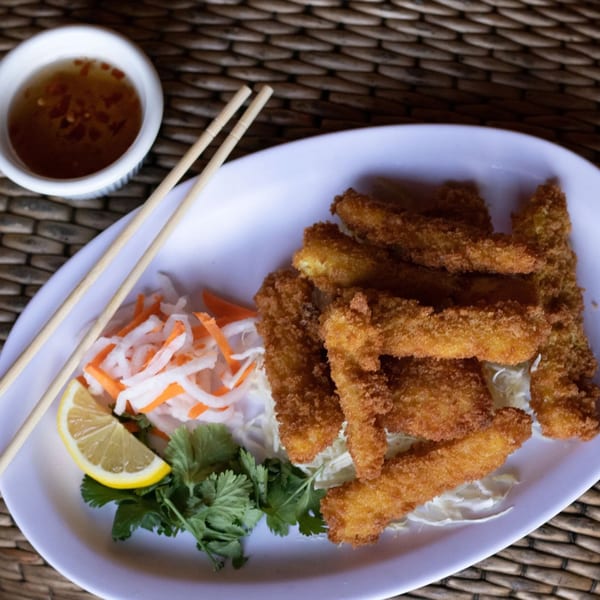 Crispy fried shrimp with pickled vegetables, lemon, cilantro, and dipping sauce on a white plate.