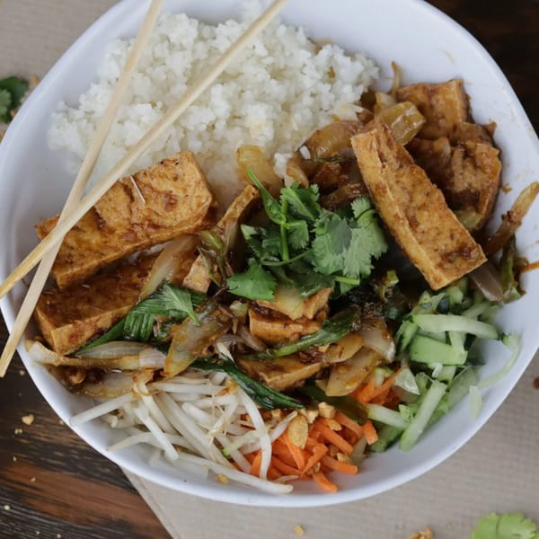 A white bowl of Vietnamese food with rice, tofu, bean sprouts, carrots, cucumbers, and cilantro.