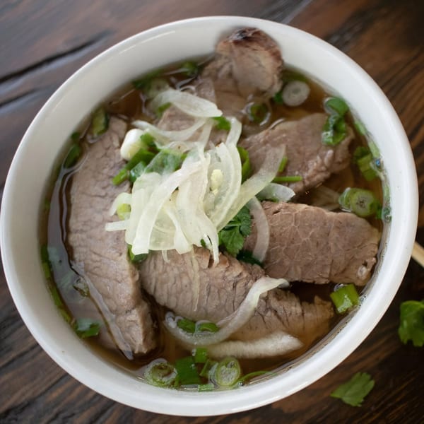 Close-up of a bowl of Pho Tre Bien's Vietnamese pho with beef, onions, and green herbs.