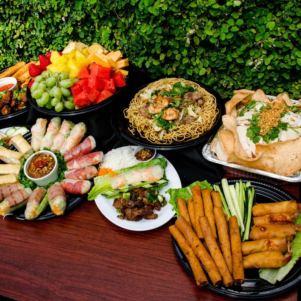 A large spread of Vietnamese dishes, including spring rolls, noodles, fruit, and other appetizers.