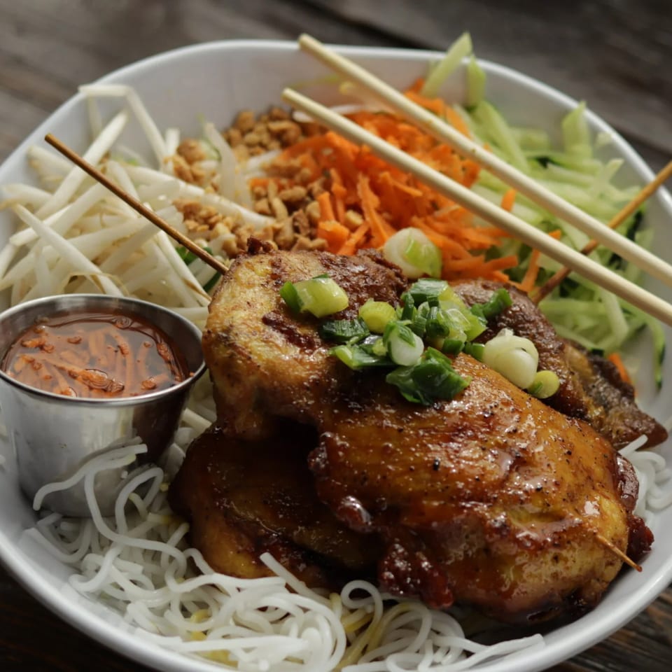 Vietnamese grilled chicken skewers with vermicelli noodles, bean sprouts, shredded carrots, and a dipping sauce.