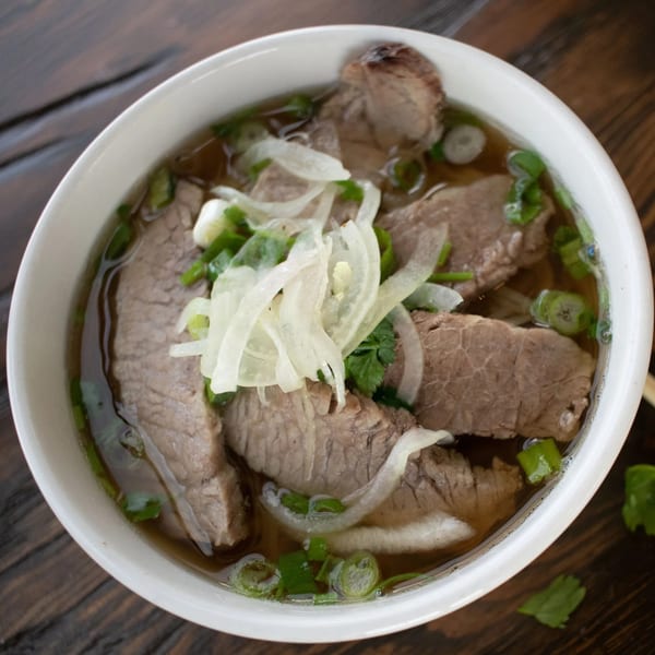 Close-up of a bowl of Pho Tre Bien's Vietnamese pho with beef, onions, and green herbs.