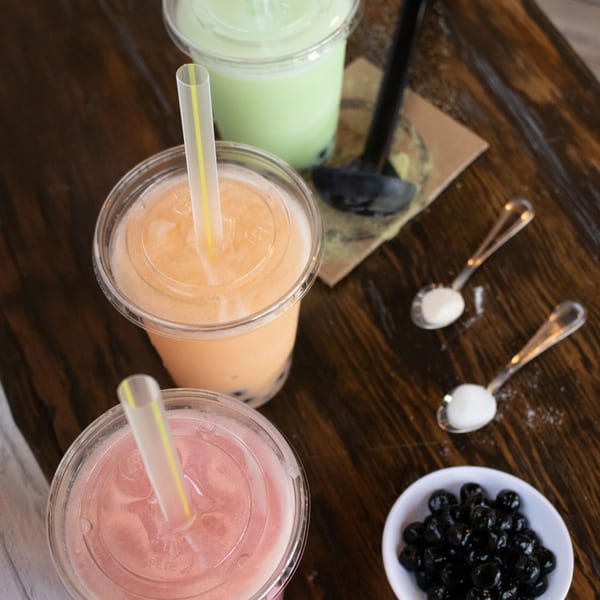 Three colorful bubble teas, tapioca pearls, and sugar on a wooden table.
