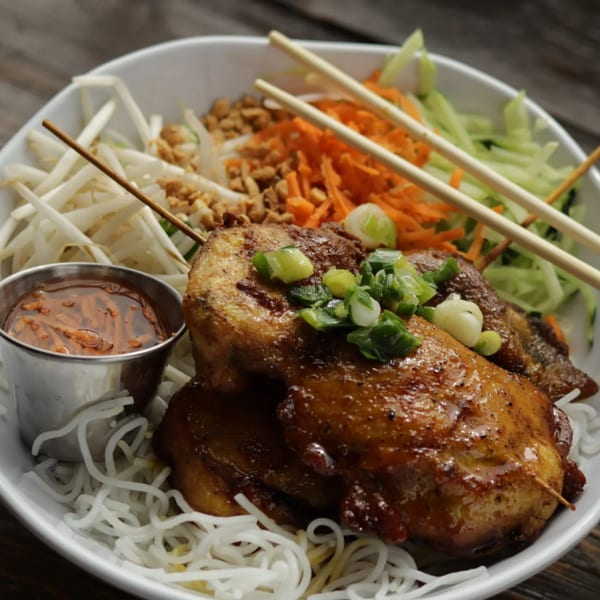 Vietnamese grilled chicken skewers with noodles, bean sprouts, shredded carrots, and a side of sauce.