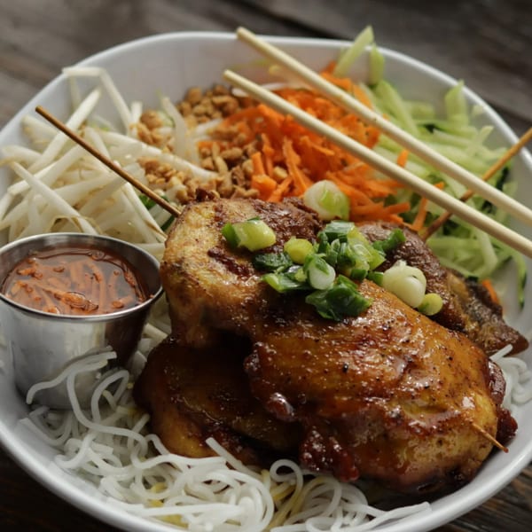 Vietnamese grilled chicken skewers with vermicelli noodles, bean sprouts, carrots, and a side sauce.